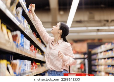 Young caucasian housewife takes food from upper shelve. Side view. Showcase at background. Concept of shopping in grocery store and consumerism. - Shutterstock ID 2288141553