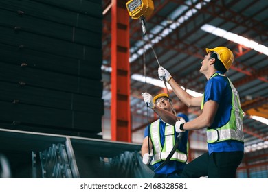 Young caucasian industrial worker holds belt for lift heavy load on hoist of crane in steel factory. - Powered by Shutterstock