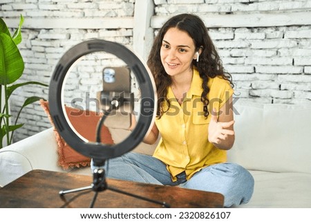 A young Caucasian influencer, creatively recording a vlog on her sofa with a ring light and mobile, sharing inspiration and connecting online.