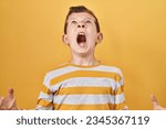 Young caucasian kid standing over yellow background crazy and mad shouting and yelling with aggressive expression and arms raised. frustration concept. 