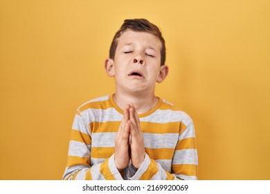 Young Caucasian Kid Standing Over Yellow Background Begging And Praying With Hands Together With Hope Expression On Face Very Emotional And Worried. Begging. 