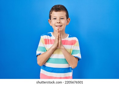 Young Caucasian Kid Standing Over Blue Background Praying With Hands Together Asking For Forgiveness Smiling Confident. 