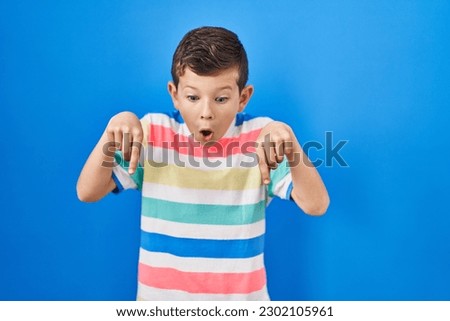 Young caucasian kid standing over blue background pointing down with fingers showing advertisement, surprised face and open mouth 