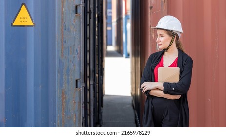 Young Caucasian Lady In Suit With White Helmet Stands Next To Cargo Container In A Logistic Shipyard. Young Female Trainee Checks Container Stocks