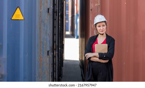 Young Caucasian Lady In Suit With White Helmet Stands Next To Cargo Container In A Logistic Shipyard. Young Female Trainee Checks Container Stocks