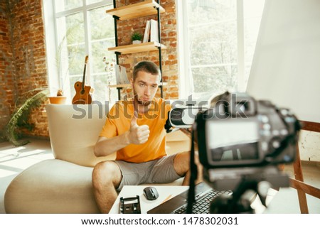 Young caucasian male blogger with professional equipment recording video review of VR glasses at home. Blogging, videoblog, vlogging. Man evaluates virtual reality headset while streaming live.