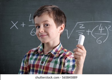 Young Caucasian Male Child Is A Maths Genius With Chalk In His Hand In Front Of Blackboard With Mathematical Problem