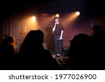 Young Caucasian male comedian performing his stand-up monologue on a stage of a small venue