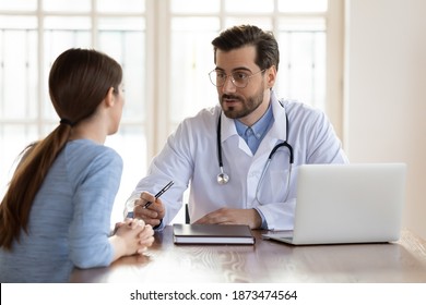 Young Caucasian Male Doctor Consult Female Patient At Meeting In Private Hospital Or Clinic. Man GP Or Physician In White Medical Uniform Have Consultation With Woman Client. Healthcare Concept.