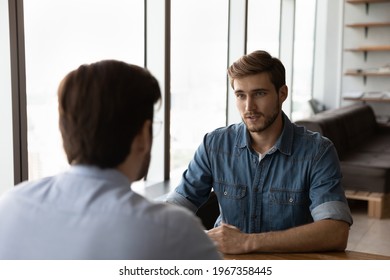 Young Caucasian male employee or worker talk speak with colleague or coworker at team meeting in office. Businessmen or business partners have negotiations at workplace. Employment concept. - Powered by Shutterstock