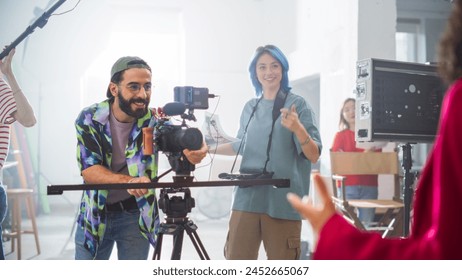 Young Caucasian Male And Female Filmmakers Collaborate On A Film Set, Adjusting Camera Equipment With Enthusiasm, Surrounded By Diverse Crew Members In A Bright, Modern Studio Environment. - Powered by Shutterstock