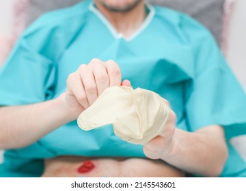 Young caucasian male patient in medical disposable pajamas puts sterile surgical white gloves on his hands to replace the coloplast after surgery at home,  side view. Concept of medicine, abdominal di