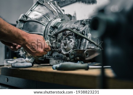 Young caucasian male is seen wrenching an automatic gearbox of an old vintage car. Tune up or checkup of a vintage car.