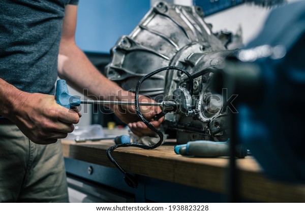 Young\
caucasian male is seen wrenching an automatic gearbox of an old\
vintage car. Tune up or checkup of a vintage\
car.