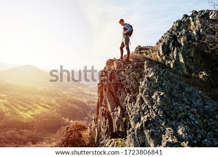 Young caucasian male traveler on high top of rock looking at valley enjoying wild environment landscape during sunset. Discovery, Travel, Adventure