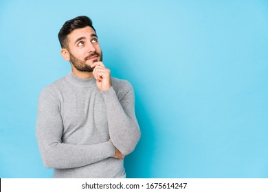 Young caucasian man against a blue background isolated looking sideways with doubtful and skeptical expression.