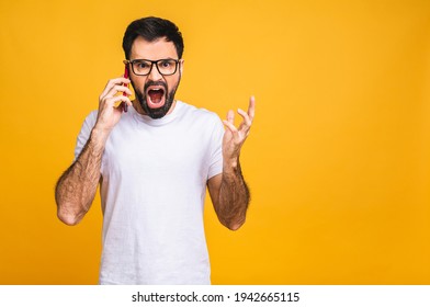 Young Caucasian Man Angry, Frustrated And Furious With His Mobile Phone, Angry With Customer Service. Isolated Over Yellow Background.