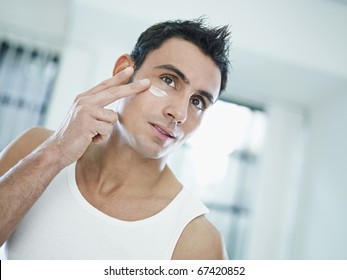 Young Caucasian Man Applying Eye Cream On Face. Horizontal Shape, Front View, Head And Shoulders