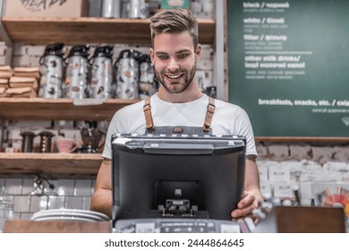 Young caucasian man in apron working with cash box in coffee shop behind the counter. Male worker, barista, waiter, manager, administrator checking order on digital cash register. Business concept. - Powered by Shutterstock