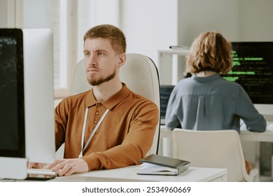 Young Caucasian man with beard on face sitting at office desk programming on desktop computer - Powered by Shutterstock