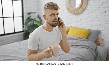 A young caucasian man with blue eyes and a beard having a phone conversation while holding a mug in a modern bedroom. - Powered by Shutterstock