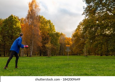 Young caucasian man in blue jacket playing disc golf on autumn play course with basket