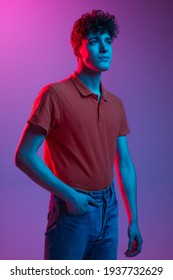 Young Caucasian man in bright clothes red shirt   jeans posing isolated multicolored background in neon light  Concept human emotions  facial expression  youth culture  Copy space for ad 