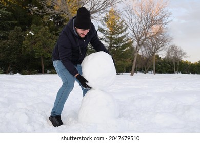 Young Caucasian Man Carrying A Big Snowball To Make Snowman.