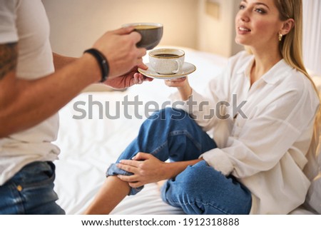 Young Caucasian man in casual clothes handing a hot beverage to his lovely female spouse