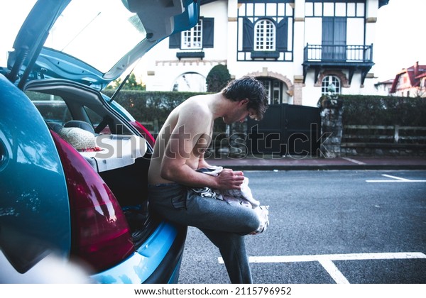 Young caucasian man changing clothes on the\
car trunk after surfing at the\
beach.