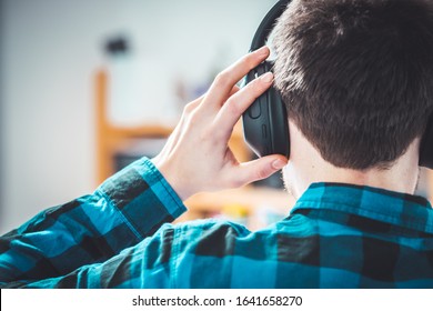 Young Caucasian Man With Checked Blue Shirt Is Listing To Music With Wireless Headphones. Back Of The Head.