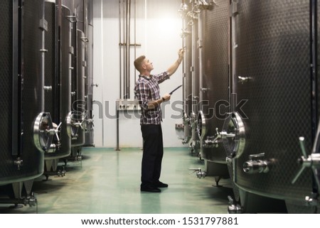 Young Caucasian man checking large steel barrels in winery. Food industry, grape wine making concept