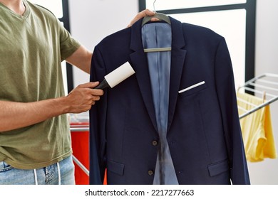 Young Caucasian Man Cleaning Jacket Using Pet Hair Roller At Laundry Room