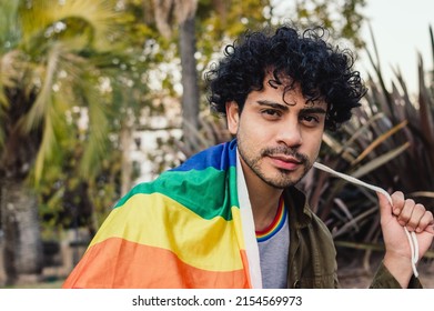 young caucasian man, with curlers and beard, outdoors smiling wrapped in pride flag looking at camera, copy space.
