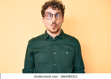 Young caucasian man with curly hair wearing casual clothes and glasses making fish face with lips, crazy and comical gesture. funny expression.  - Powered by Shutterstock