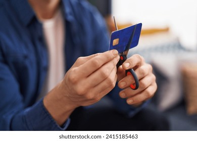 Young caucasian man cutting credit card sitting on sofa at home - Powered by Shutterstock