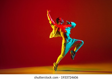 Young Caucasian man dancing hip-hop isolated over red background in neon light