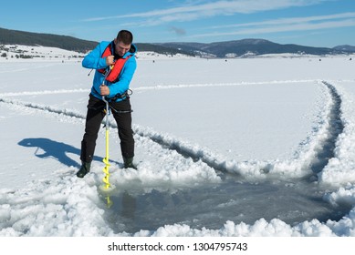 Young Caucasian Man Drilling The Ice On A Frozen Lake With Ice Auger Drill. Selective Focus 