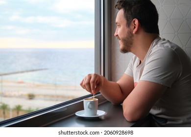 Young Caucasian Man Drink Coffee Look At The Sunrise And Sea Throw The Window.