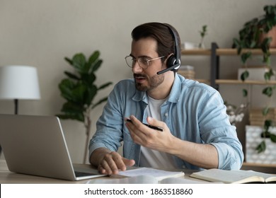 Young Caucasian man in earphones sit at desk in home office have online video training or meeting on computer. Millennial male in headphones work distant talk speak on webcam digital call on laptop. - Shutterstock ID 1863518860