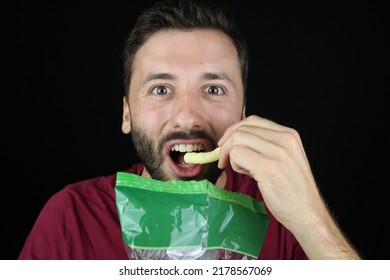 Young Caucasian Man Eating Chips, Black Background  