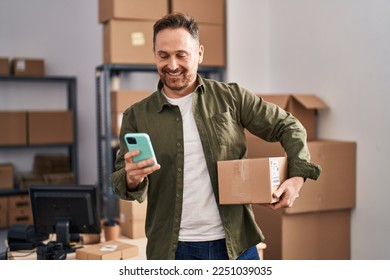 Young caucasian man ecommerce business worker using smartphone holding package at office
