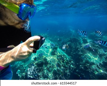 Joven caucásico hombre libre buceador closeup usando máscara de buceo tomando fotos de peces tropicales con cámara de acción bajo el agua. Arrecife de coral isla Koh Tao, Tailandia.