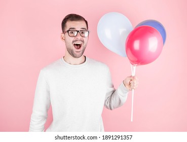 Young caucasian man holding balloons with surprised expression and celebrating a brithday isolated in a pink background