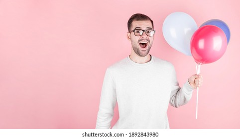 Young caucasian man holding balloons with surprised expression and celebrating a brithday isolated in a pink background
