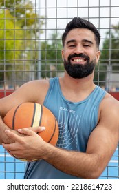 Young Caucasian Man Holding Basketball Ball And Looking At The Camera At City Public Basketball Court