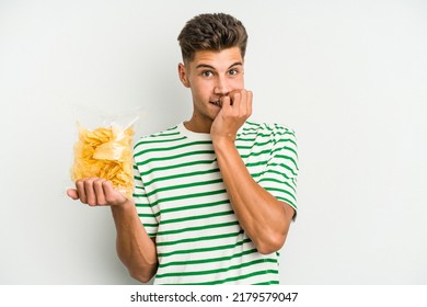 Young caucasian man holding crisps isolated on white background biting fingernails, nervous and very anxious.