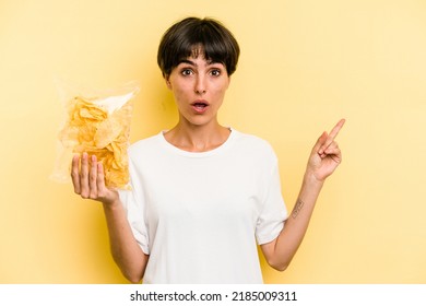 Young caucasian man holding crisps isolated on yellow background pointing to the side