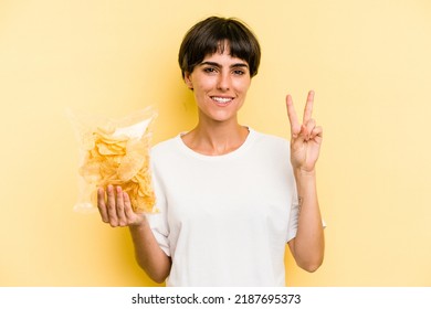 Young caucasian man holding crisps isolated on yellow background showing number two with fingers.