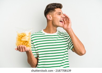Young caucasian man holding crisps isolated on white background shouting and holding palm near opened mouth.